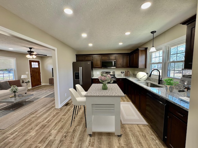 kitchen featuring light wood-style flooring, appliances with stainless steel finishes, a sink, a kitchen island, and dark brown cabinets