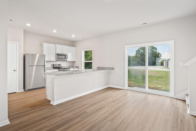 kitchen featuring light wood finished floors, white cabinets, appliances with stainless steel finishes, a peninsula, and recessed lighting