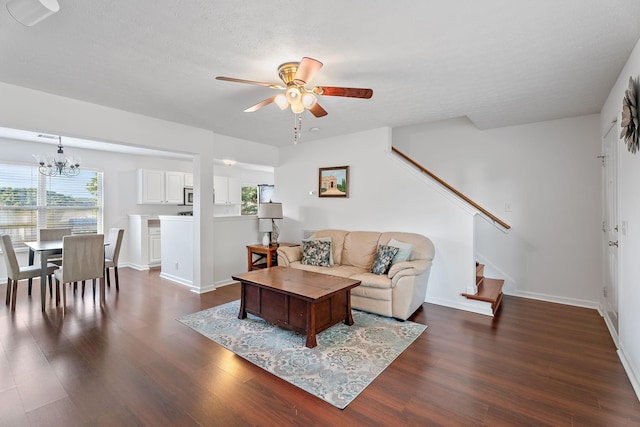 living area featuring dark wood-style floors, stairway, ceiling fan with notable chandelier, and baseboards