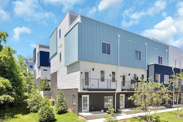 exterior space featuring a balcony, a yard, board and batten siding, and brick siding