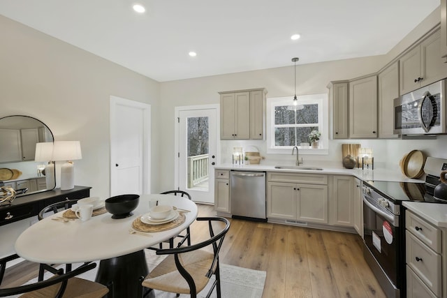 kitchen with a sink, light wood-style floors, light countertops, appliances with stainless steel finishes, and decorative light fixtures