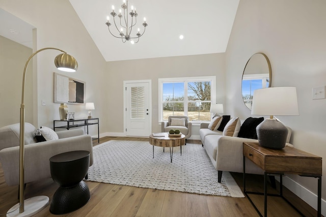 living area featuring high vaulted ceiling, an inviting chandelier, wood finished floors, and baseboards