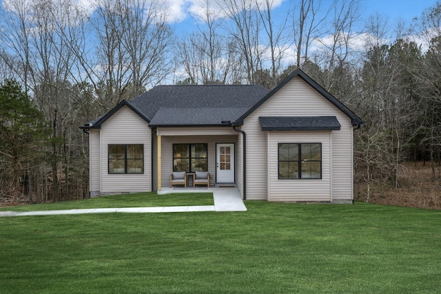 view of front facade with a shingled roof, a front yard, and a patio