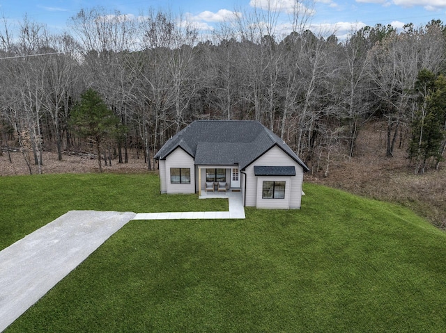 view of front of home with a shingled roof, a front yard, a forest view, and an outbuilding