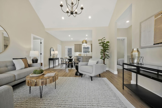 living area with light wood finished floors, recessed lighting, a chandelier, high vaulted ceiling, and baseboards