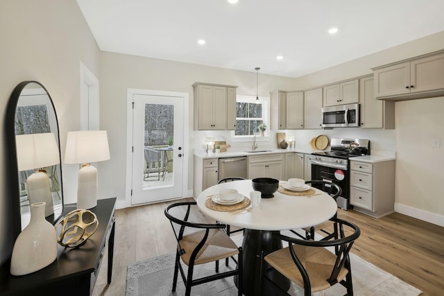 kitchen with light wood finished floors, baseboards, appliances with stainless steel finishes, light countertops, and a sink