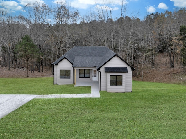 view of front of house featuring a front lawn, a shingled roof, and a wooded view