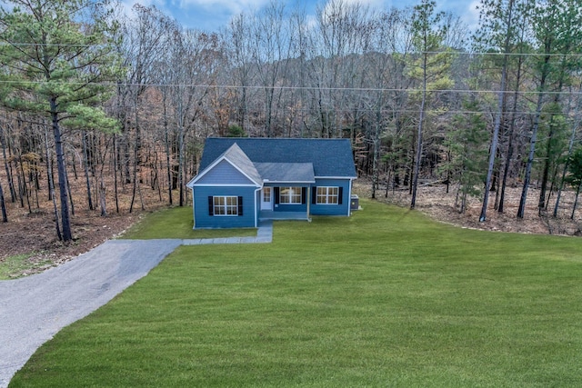 view of front of property with driveway, a front lawn, a shingled roof, and a wooded view