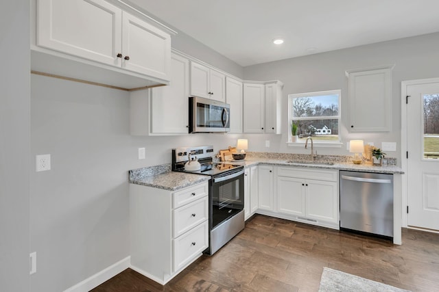 kitchen with white cabinets, dark wood finished floors, appliances with stainless steel finishes, light stone countertops, and a sink