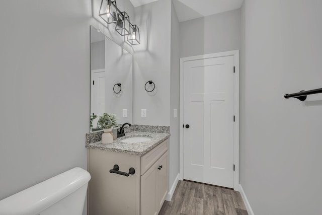 bathroom with wood finished floors, vanity, toilet, and baseboards