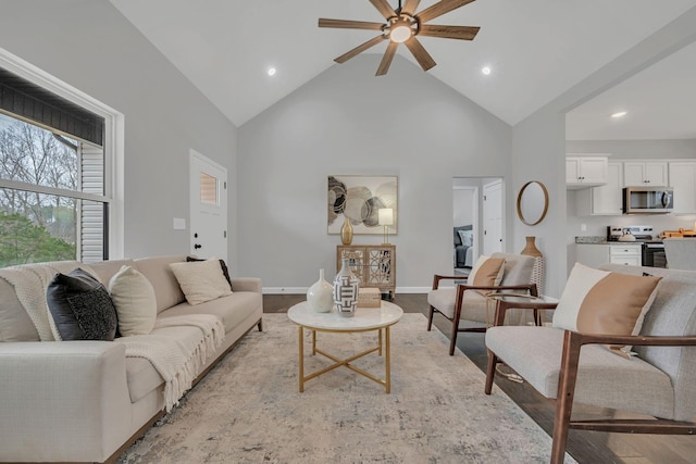 living area with high vaulted ceiling, ceiling fan, light wood-style flooring, and baseboards