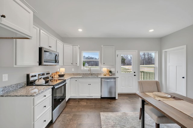 kitchen with dark wood-type flooring, light stone countertops, stainless steel appliances, white cabinetry, and a sink