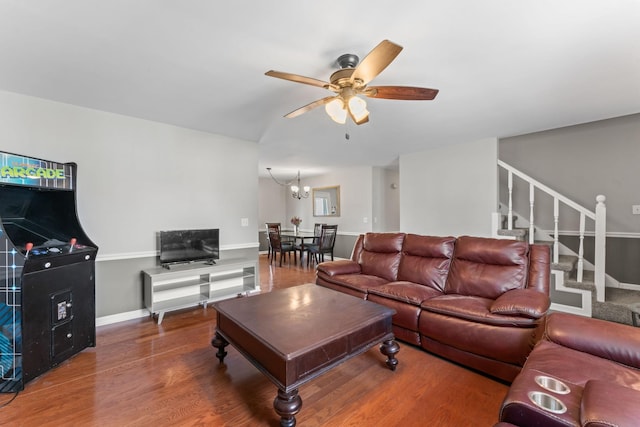 living area featuring baseboards, stairway, wood finished floors, and ceiling fan with notable chandelier