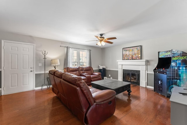 living room with a glass covered fireplace, ceiling fan, baseboards, and wood finished floors