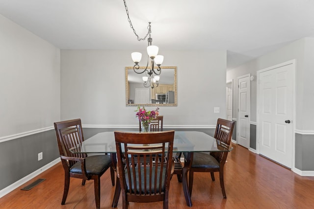 dining room featuring an inviting chandelier, wood finished floors, visible vents, and baseboards