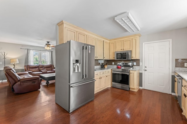 kitchen featuring cream cabinets, open floor plan, appliances with stainless steel finishes, backsplash, and dark wood finished floors