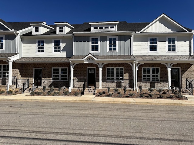 townhome / multi-family property with board and batten siding, covered porch, brick siding, and a standing seam roof