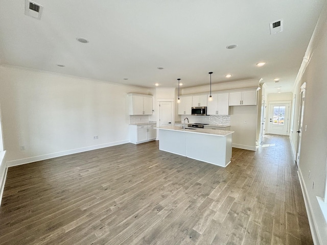 kitchen with crown molding, tasteful backsplash, stainless steel microwave, white cabinetry, and wood finished floors