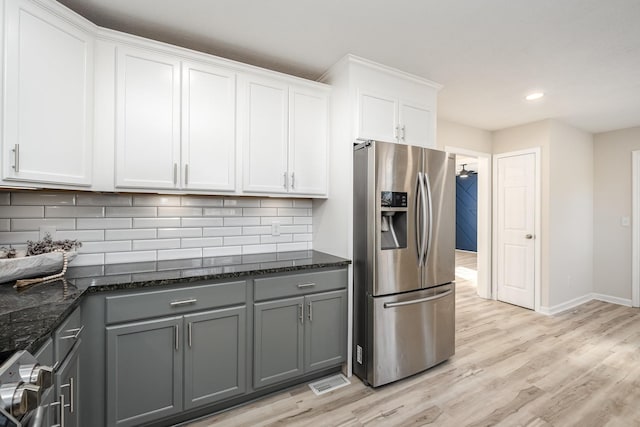 kitchen with dark stone counters, decorative backsplash, stainless steel fridge with ice dispenser, gray cabinets, and light wood-style floors