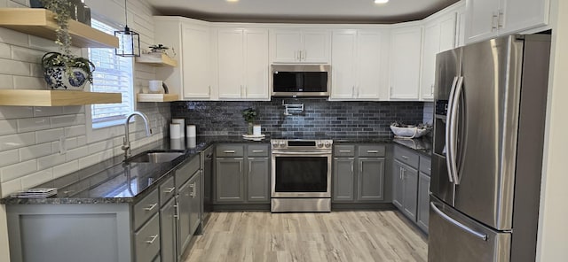 kitchen featuring light wood finished floors, appliances with stainless steel finishes, gray cabinets, open shelves, and a sink