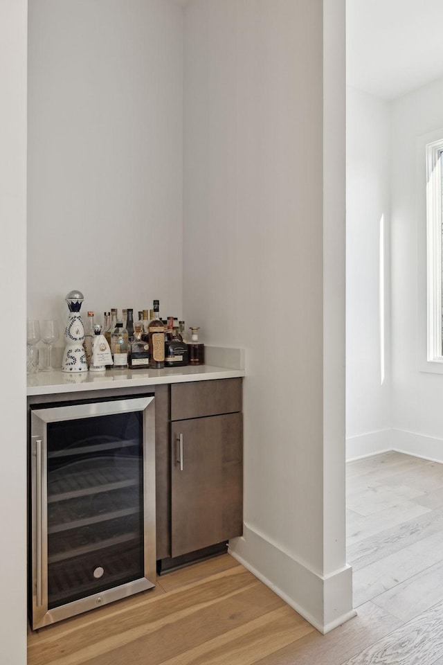 bar with beverage cooler, a dry bar, baseboards, and light wood-style floors