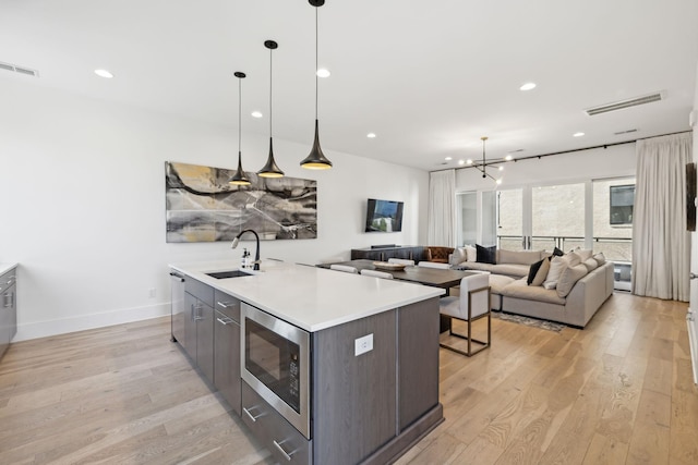 kitchen featuring a center island with sink, stainless steel appliances, visible vents, light wood-style floors, and a sink