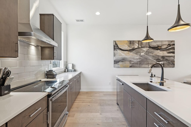 kitchen featuring light wood-style floors, a sink, stainless steel appliances, wall chimney range hood, and backsplash