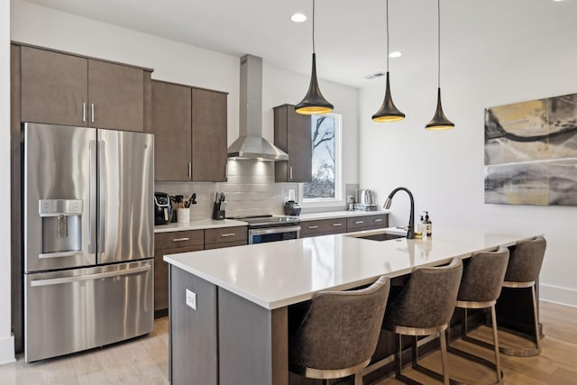 kitchen with stainless steel appliances, dark brown cabinets, light countertops, wall chimney range hood, and a sink