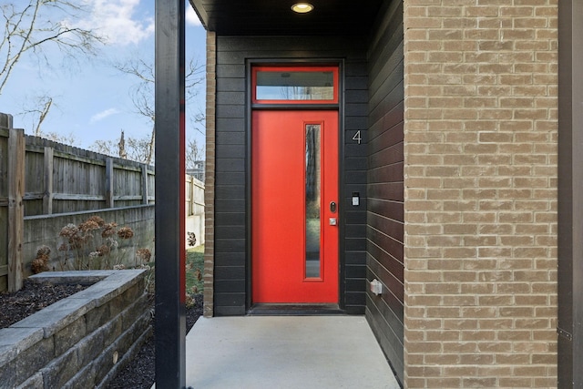 view of exterior entry with fence and brick siding