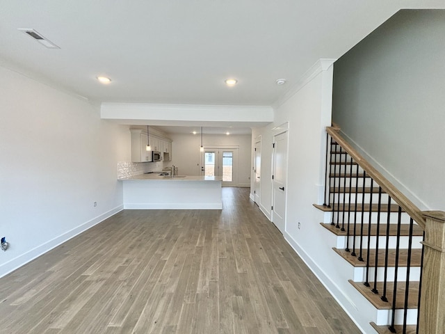 unfurnished living room featuring baseboards, visible vents, wood finished floors, stairs, and a sink