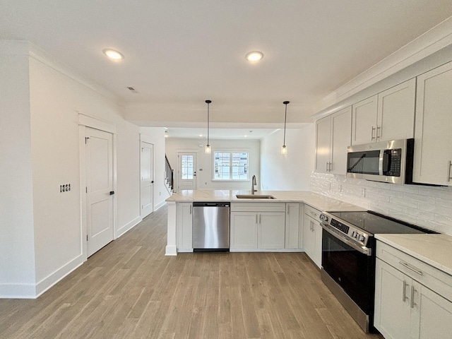 kitchen featuring decorative backsplash, a peninsula, stainless steel appliances, light wood-style floors, and a sink