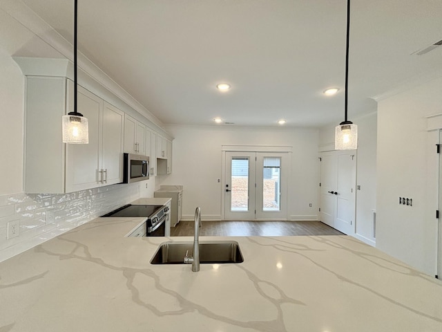 kitchen with light stone counters, ornamental molding, a sink, stainless steel appliances, and backsplash