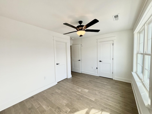 unfurnished bedroom with a ceiling fan, wood finished floors, visible vents, and baseboards