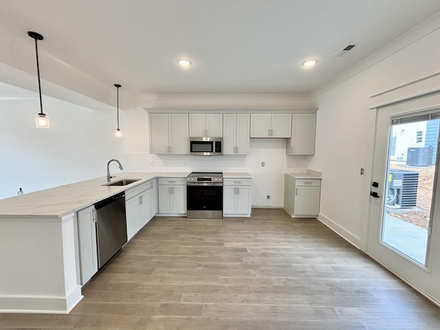 kitchen with decorative light fixtures, a peninsula, stainless steel appliances, light wood-type flooring, and a sink