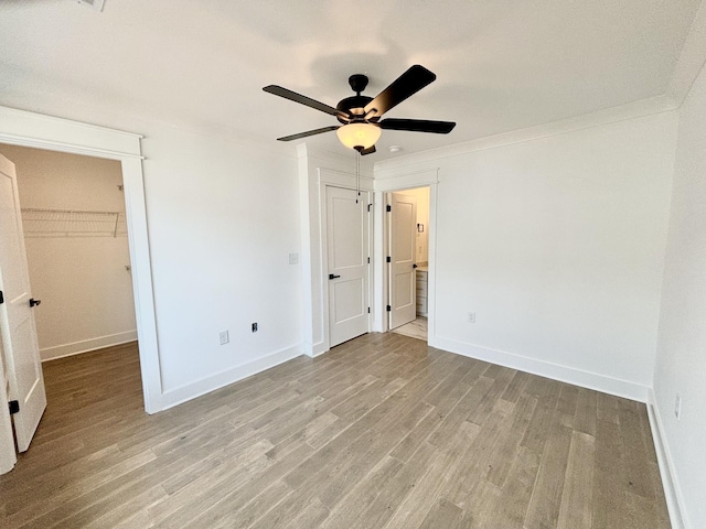 unfurnished bedroom featuring baseboards, ornamental molding, ensuite bathroom, a spacious closet, and light wood-style floors