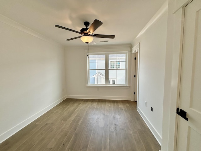 empty room featuring baseboards, crown molding, visible vents, and wood finished floors