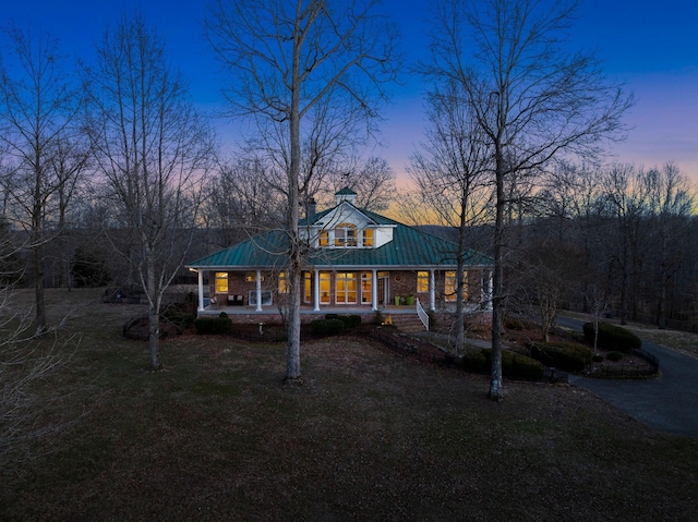 view of front of property featuring driveway, a chimney, a porch, metal roof, and a front lawn