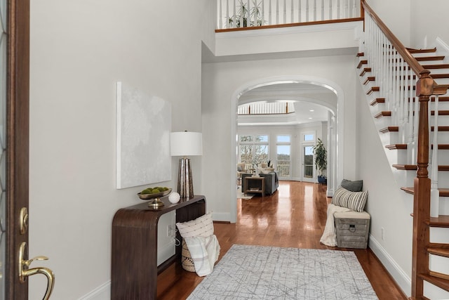 foyer entrance with arched walkways, baseboards, a high ceiling, and wood finished floors