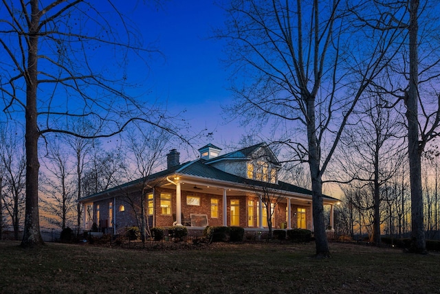 exterior space featuring metal roof, covered porch, brick siding, a yard, and a chimney