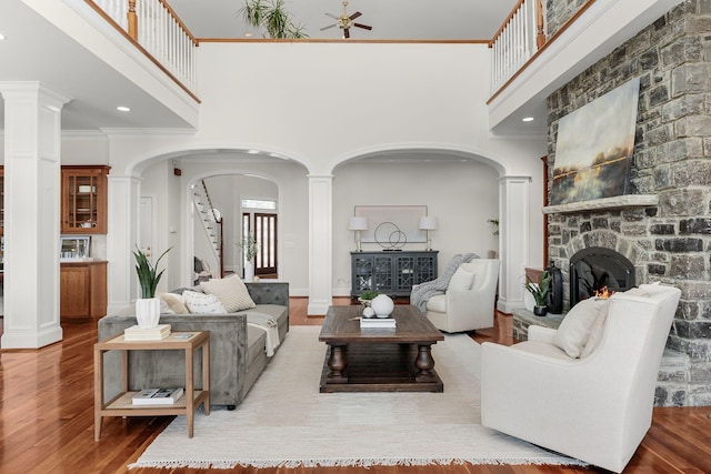 living room featuring arched walkways, crown molding, a stone fireplace, wood finished floors, and stairs