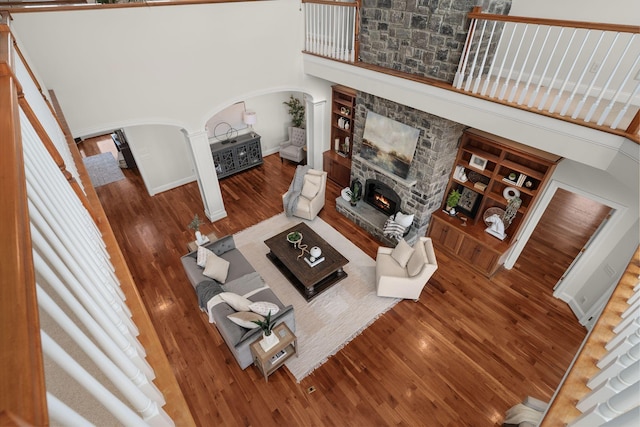 living area featuring a high ceiling, a fireplace, arched walkways, and wood finished floors