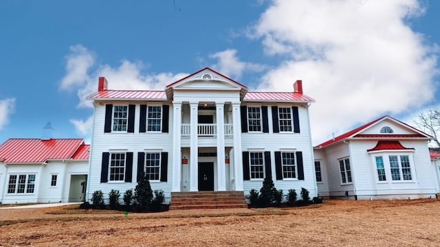 neoclassical / greek revival house featuring a standing seam roof, metal roof, a chimney, and a balcony