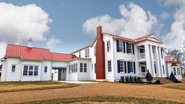 neoclassical home featuring metal roof, a chimney, a front yard, and a balcony