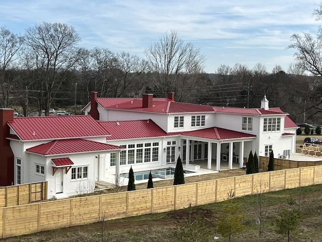 back of property featuring metal roof, a chimney, and a fenced backyard