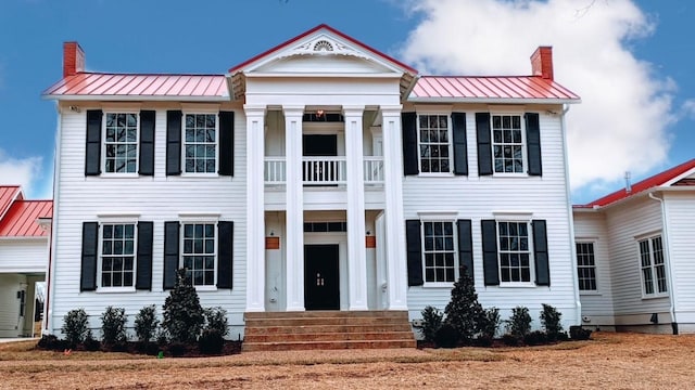 greek revival inspired property featuring a standing seam roof, metal roof, and a chimney