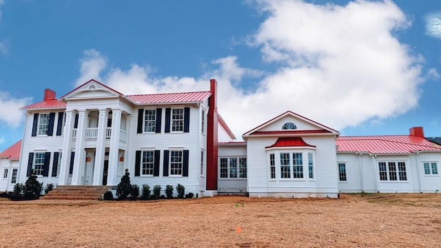 neoclassical home featuring a standing seam roof, metal roof, and a chimney