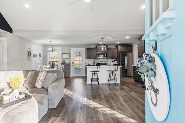 living room with ceiling fan with notable chandelier, dark wood-type flooring, and recessed lighting