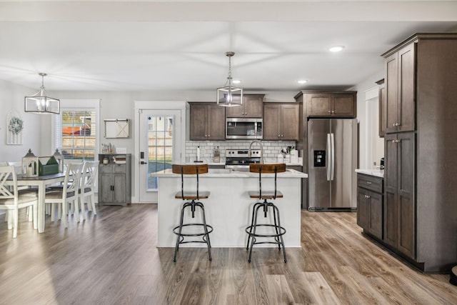 kitchen with tasteful backsplash, hanging light fixtures, appliances with stainless steel finishes, dark brown cabinets, and wood finished floors