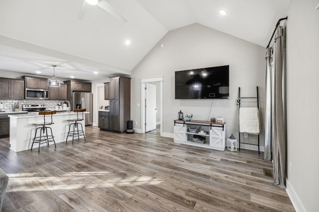 living room with high vaulted ceiling, ceiling fan, baseboards, and wood finished floors