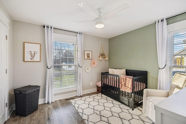 bedroom featuring a crib, wood finished floors, a ceiling fan, and baseboards